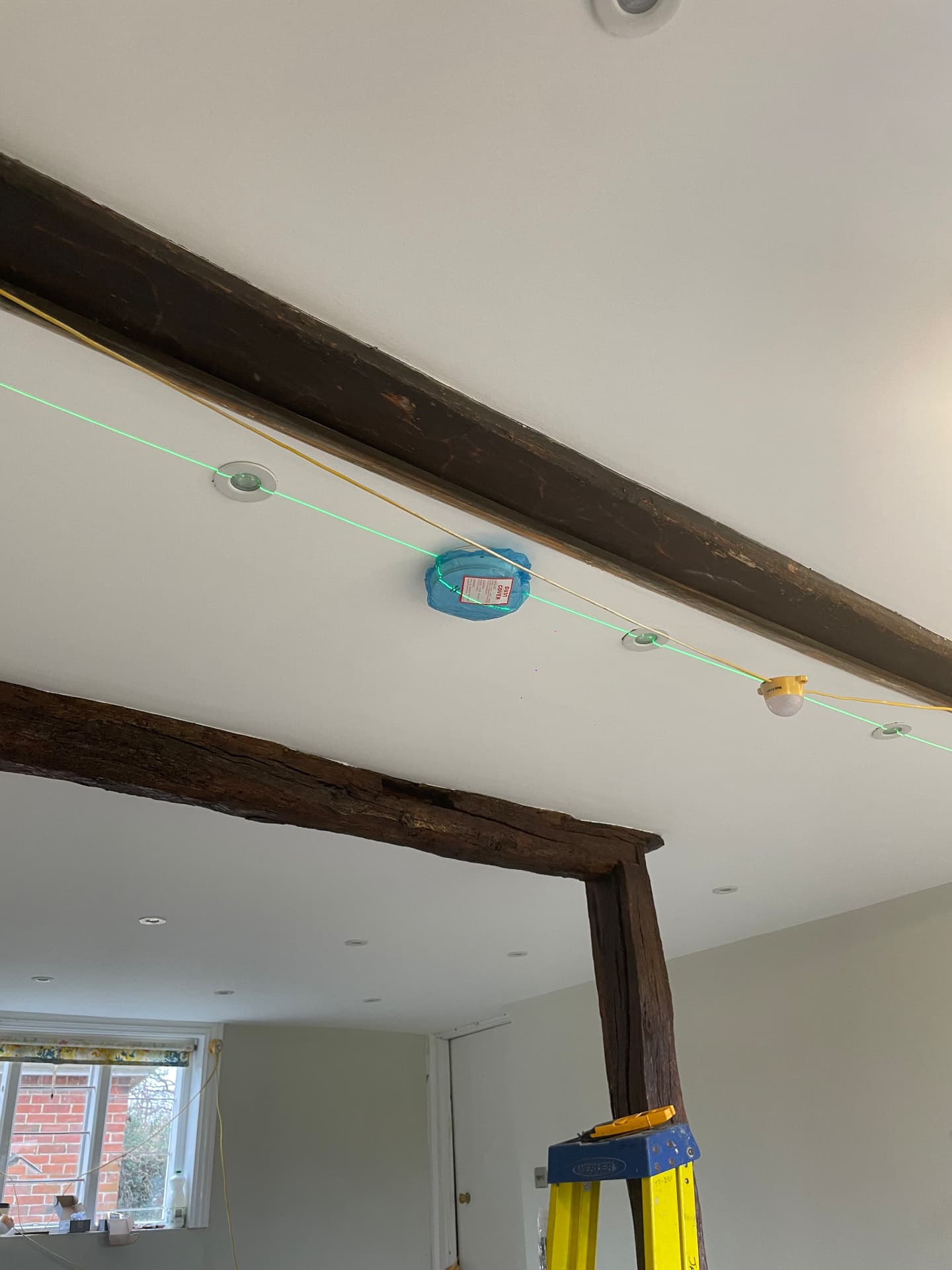 Downlights set out with a laser line around exposed beams during a lighting install