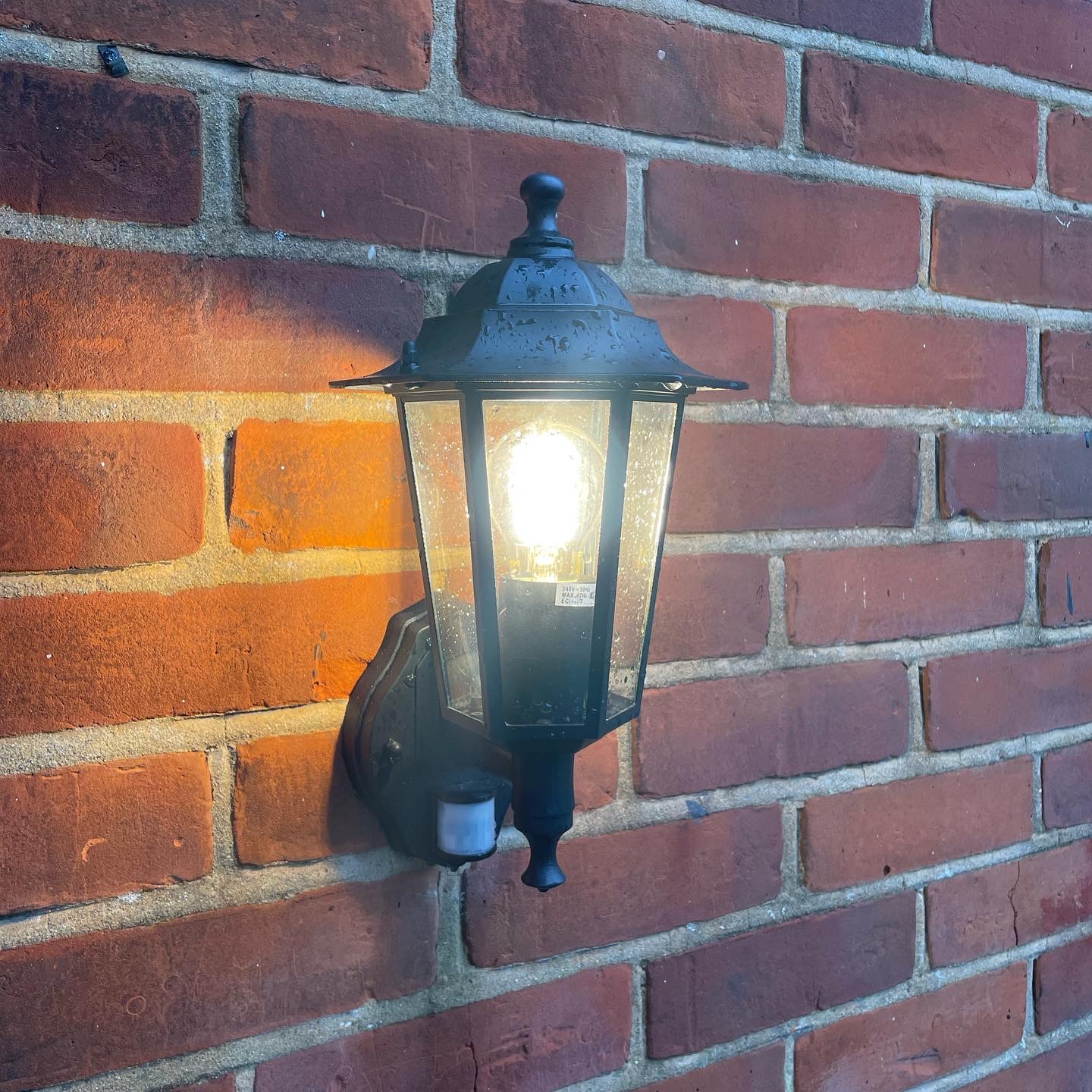 Outdoor lantern wall light with PIR sensor installed on a brick wall
