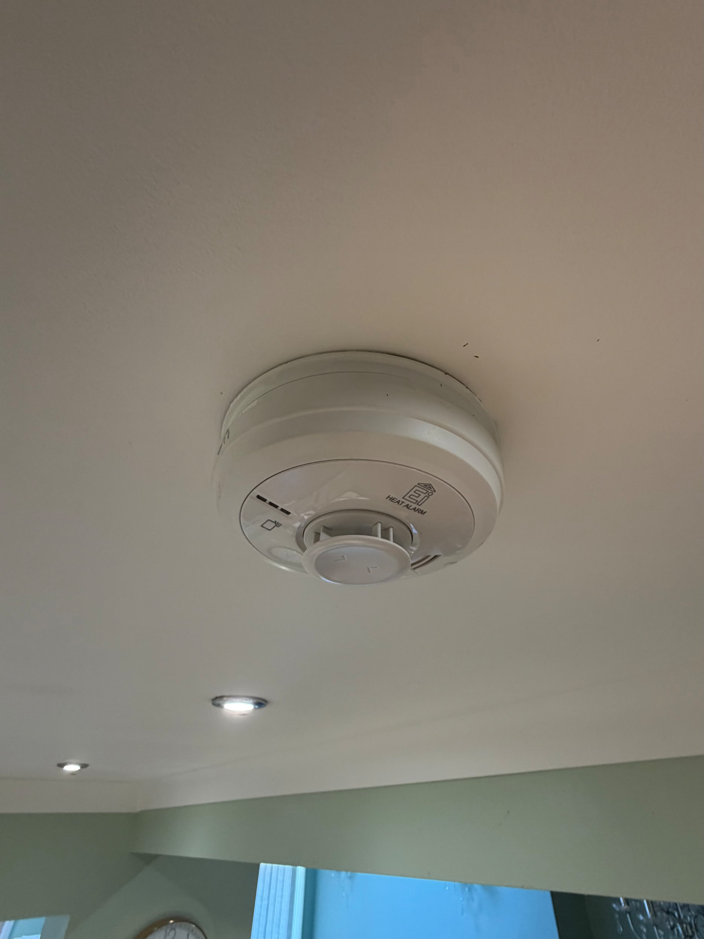 Mains-wired heat alarm installed on a hallway ceiling alongside downlights