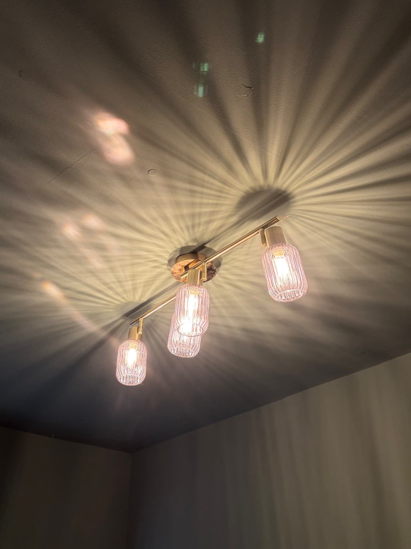 Brass triple spotlight bar with ribbed glass shades fitted to a ceiling