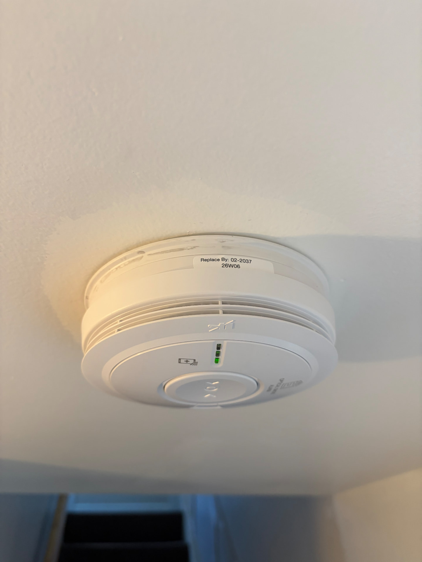 Smoke alarm installed on a landing ceiling with replacement date label