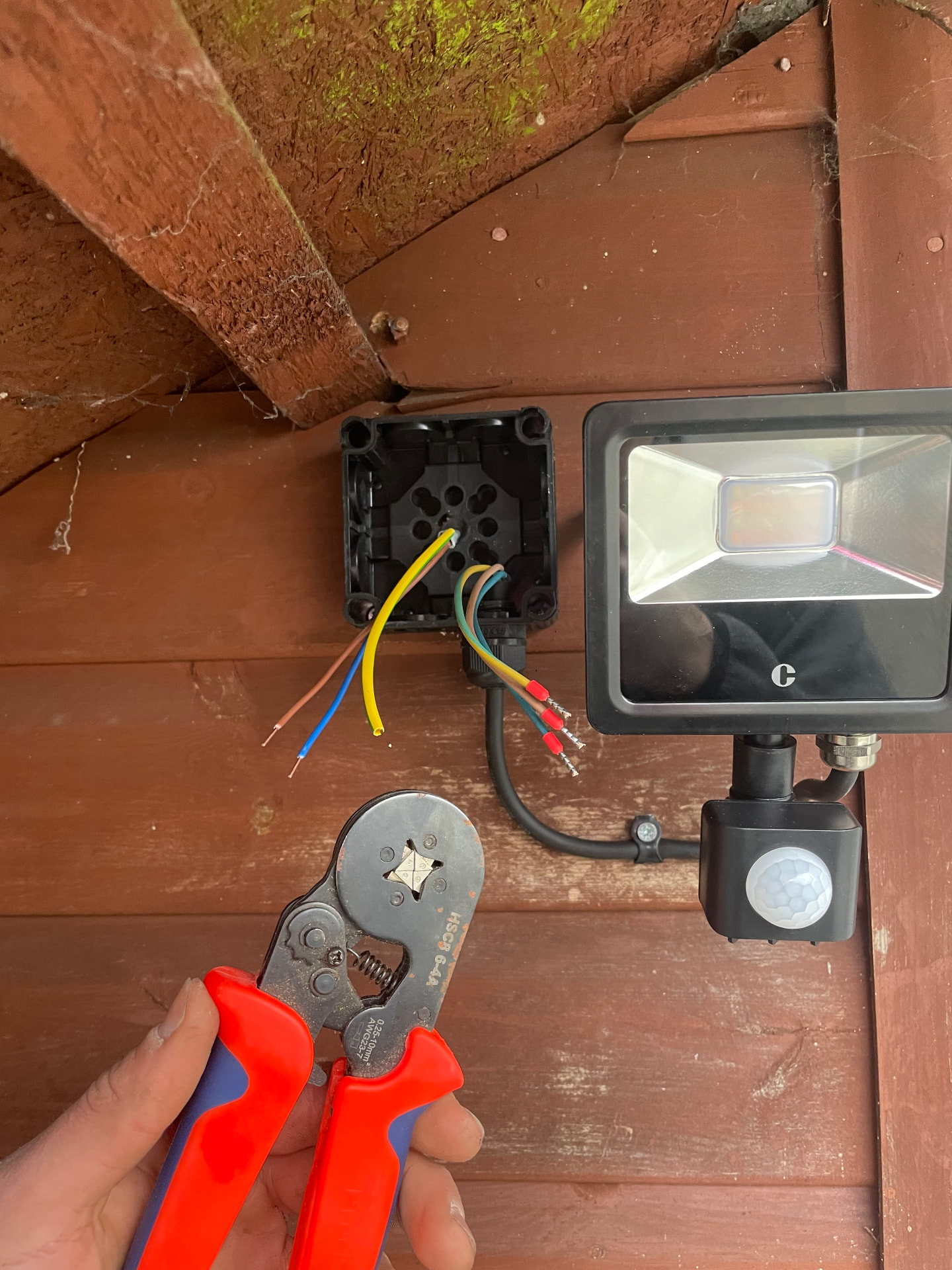PIR security floodlight being wired and installed on an outbuilding