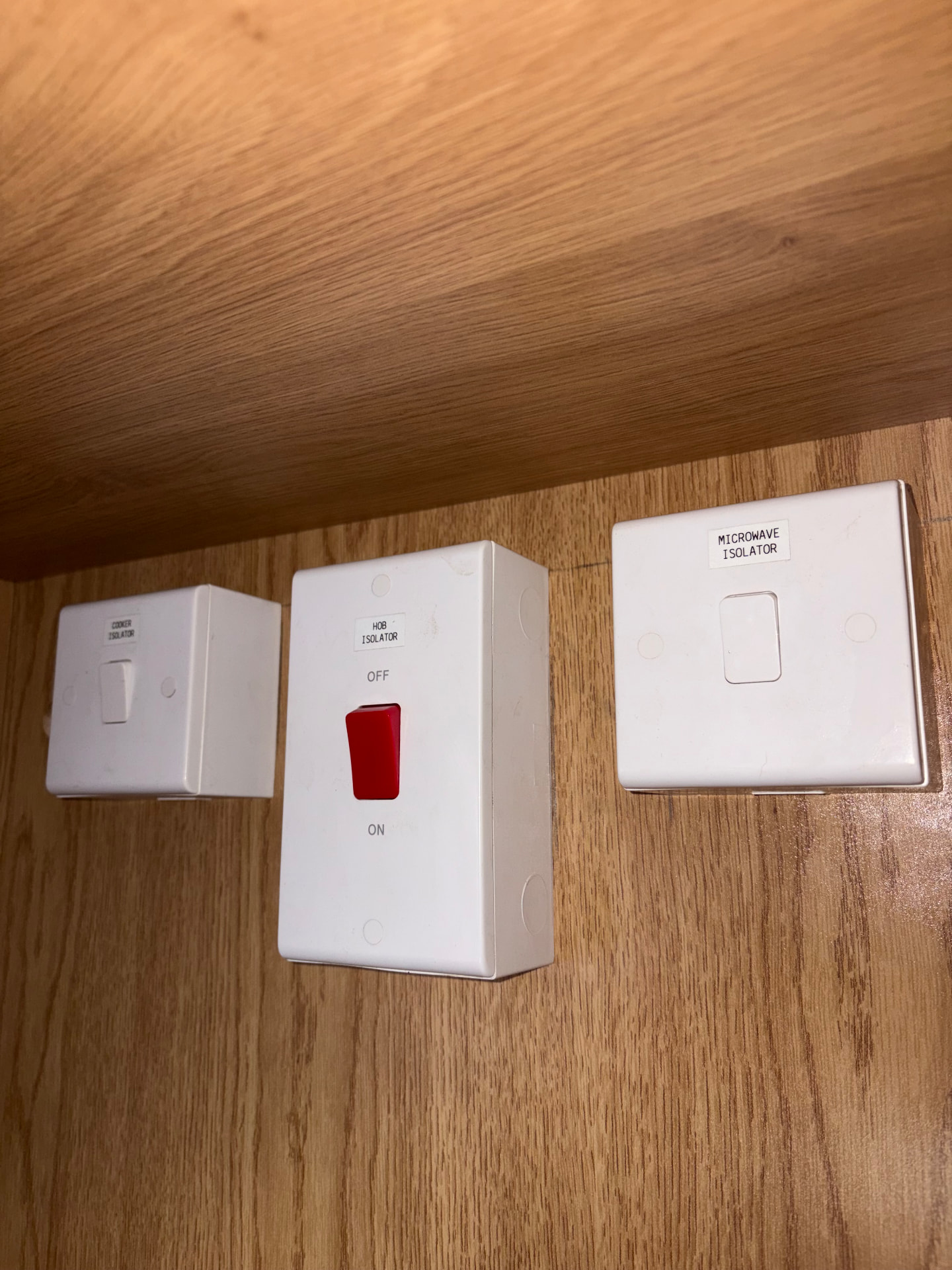 Labelled cooker, hob and microwave isolator switches inside a kitchen unit